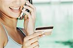 Close-up of a young woman holding a credit card and talking on a mobile phone