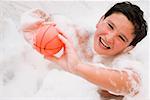 Portrait d'un garçon tenant une boule dans une baignoire et souriant