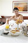 Mitte erwachsener Mann sitzt auf dem Bett mit Frühstück vor ihm