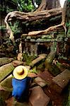 High angle view of a man crouching on a stone in front of a temple, Ta Prohm Temple, Angkor Siem Reap, Cambodia