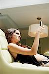 Seitenansicht einer jungen Frau liegend auf der Couch und hält ein Mobiltelefon