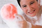 Portrait d'un garçon tenant une boule dans une baignoire et souriant