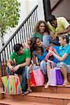 Three teenage girls and two young men sitting on steps and holding shopping bags