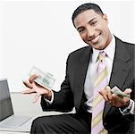 Portrait of a businessman sitting beside a laptop and holding paper currency