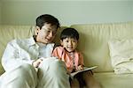Father and son sitting on sofa, reading book