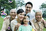 Three generation family in park blowing bubbles, portrait