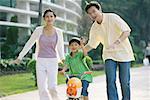 Boy riding bicycle, parents on either side, waving at camera