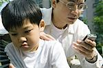 Man looking at cell phone while son looks away, frowning