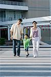 Boy crossing crosswalk, hand in hand with parents, full length