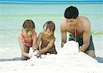 Father and two children playing in sand on beach