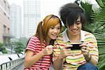 Teenage couple playing with handheld video game, outdoors