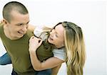 Jeune couple, l'homme holding jeune femme sur le dos, regarder par-dessus l'épaule, souriant à l'autre