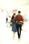 Couple walking through shopping mall, rear view, full length, blurred motion