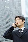 Young businessman using cell phone, looking away, office building in background