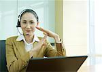 Femme d'affaires portant casque et utilisant un ordinateur portable, faisant le geste de délai d'attente