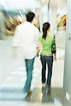 Couple walking in shopping mall, rear view, blurred motion