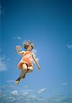 Girl jumping, sky in background, low angle view