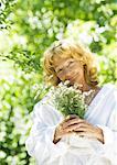 Senior woman wearing bathrobe, holding flowers, outdoors