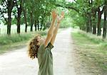 Boy standing in middle of dirt road, arms raised