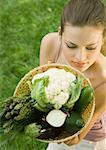 Young woman holding up basket full of vegetables