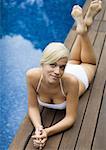 Young woman lying on deck by edge of pool