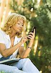 Senior woman using cell phone, laZSop on lap, outdoors