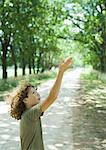 Boy standing in middle of dirt road, arm raised