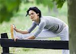 Young woman stretching leg on wooden fence