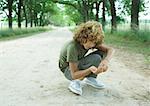 Boy crouching in middle of dirt road, looking at pebbles