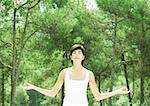 Woman standing with arms in lotus position, eyes closed, trees in background