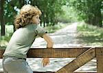 Boy hanging on fence, dirt road in background