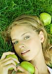 Femme couchée dans l'herbe, tenant des pommes près de visage