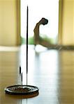 Yoga class, woman doing cobra pose, focus on incense in foreground