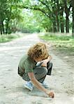 Boy crouching in middle of dirt road