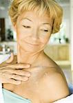 Senior woman applying moisturizer to shoulder