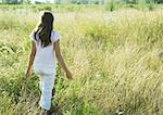 Girl walking through tall grass in field