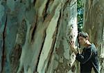 Man pressing face and hands against tree trunk