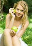 Jeune femme assise dans l'herbe, brandissant des pommes