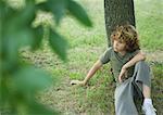 Boy sitting, leaning against tree