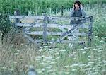 Man leaning against gate, listening to headphones