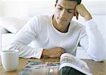 Man sitting at table, looking at book, with coffee cup