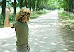 Boy standing in middle of dirt road, throwing pebbles