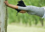 Young woman stretching against tree trunk