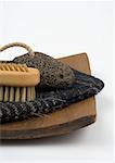 Pumice stone, nail brush, and exfoliation glove on wooden tray, partial view