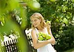 Young woman wearing white dress, holding bowl of apples