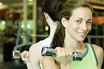 Two women lifting dumbbells, back to back
