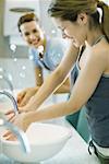 Young women splashing water in sinks in public restroom