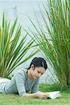 Young woman lying on grass, reading