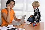 Mother phoning with a mobile phone, son (4-5 Years) sitting on a table and drawing