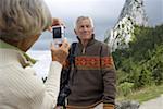 Senior adult woman taking a picture of her husband in the mountains, selective focus
